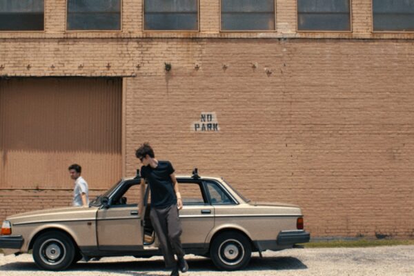 Gold Connections exiting vintage car stopped in front of brick wall marked "No Park"