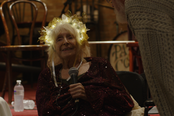 Nina Buck holds microphone, seated in front of stage wearing a glowing tiara