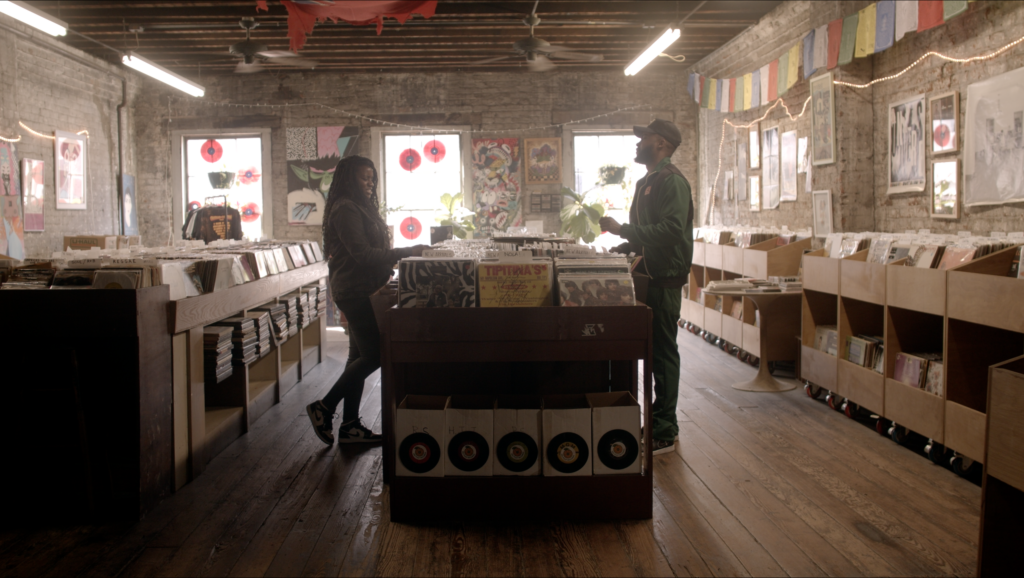 Wide shot of a couple conversing across the stacks at a record store