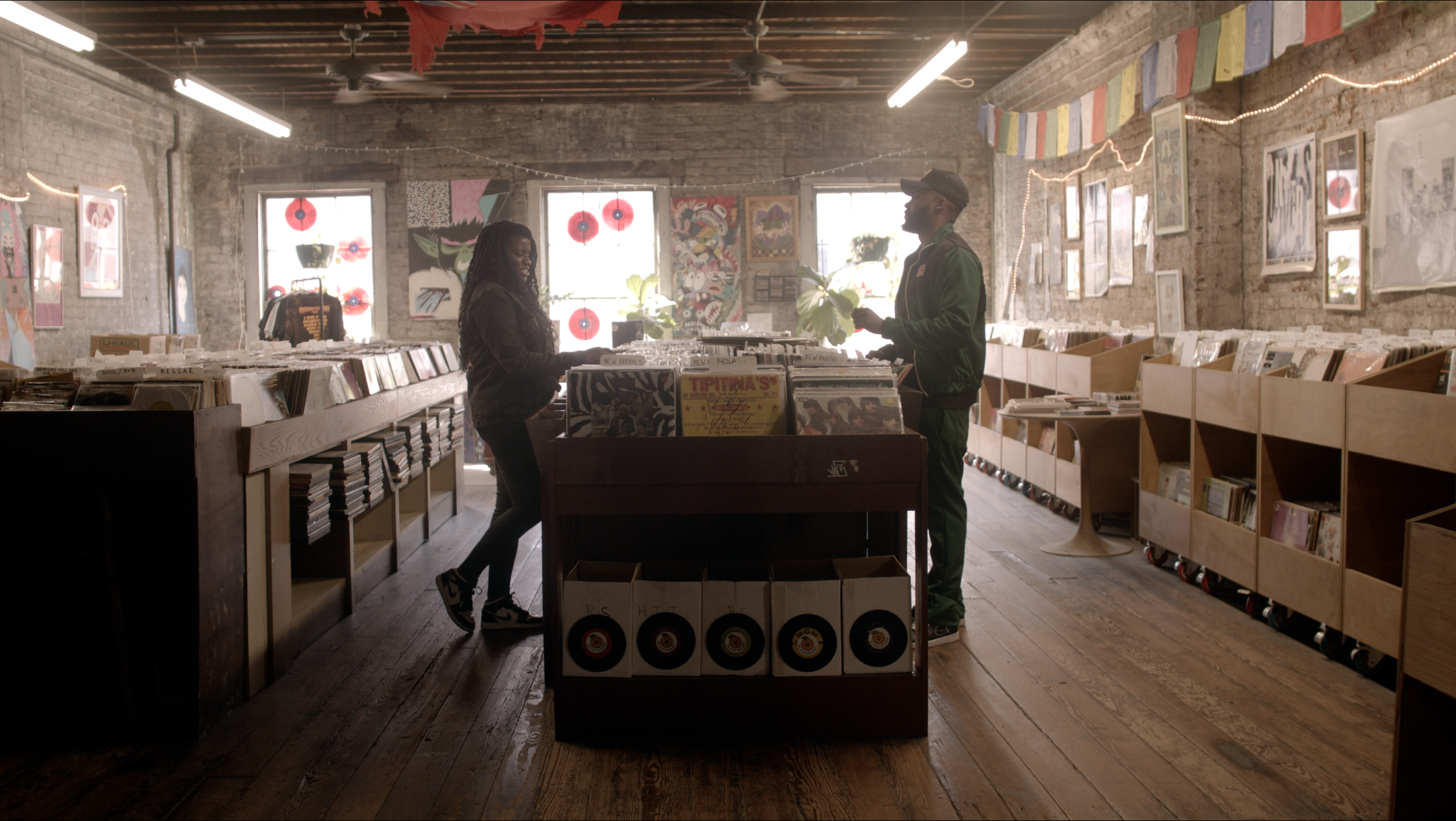 Wide shot of a couple conversing across the stacks at a record store