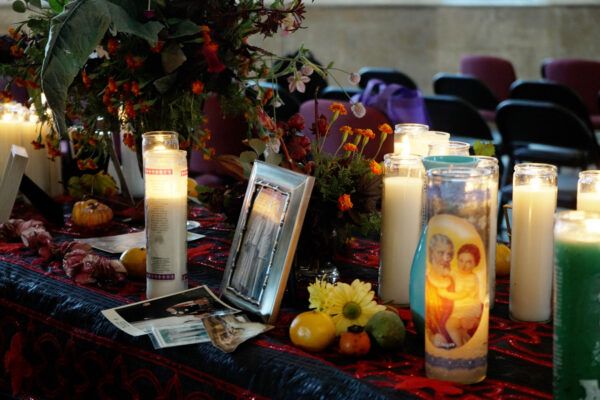 Tabletop altar with lit candles, photos, flowers, and fruit